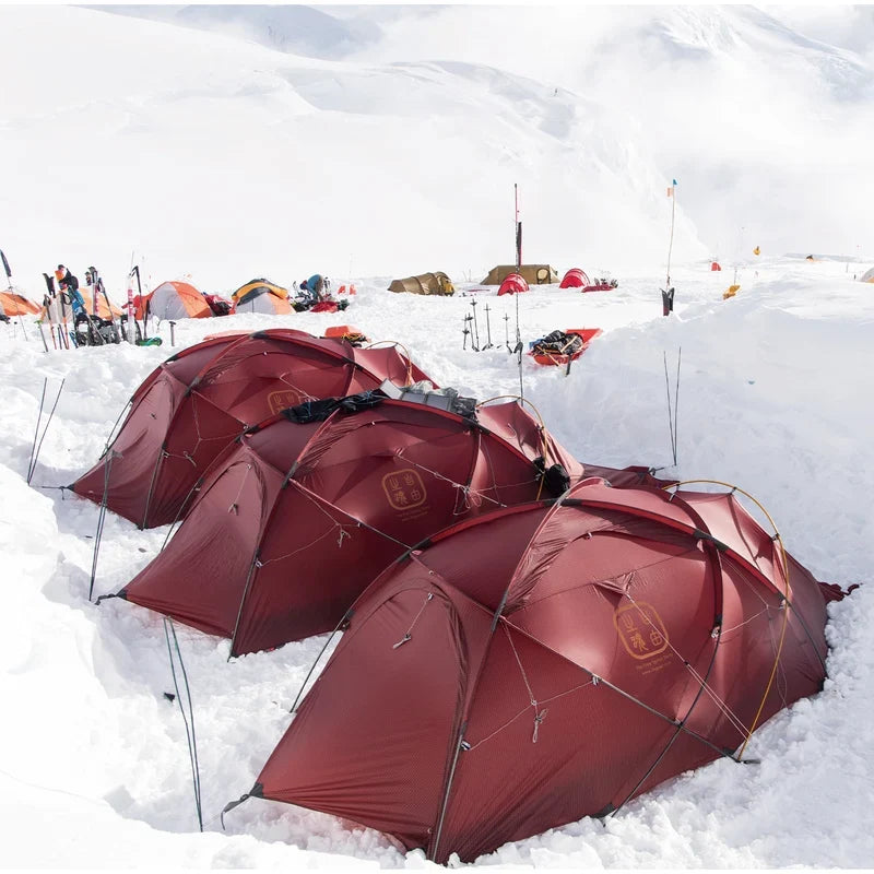 The Free Spirits Whisperwind S red tents pitched at a snowy high-altitude basecamp, expedition camp under white mountains.