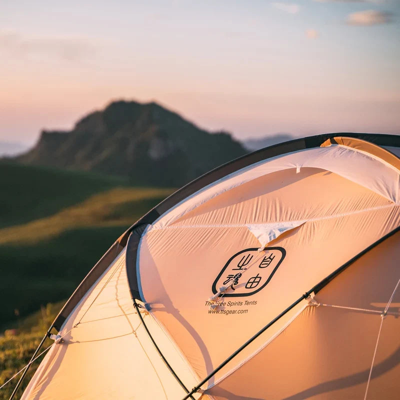 The Free Spirits Whisperwind S logo printed on the sunlit flysheet at golden hour, mountain silhouette in the background.