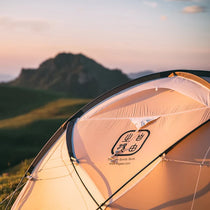 The Free Spirits Whisperwind S logo printed on the sunlit flysheet at golden hour, mountain silhouette in the background.