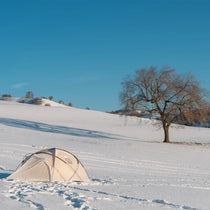 The Free Spirits Whisperwind S tent pitched on a snowy field with a bare tree, clear blue sky and low winter sun.