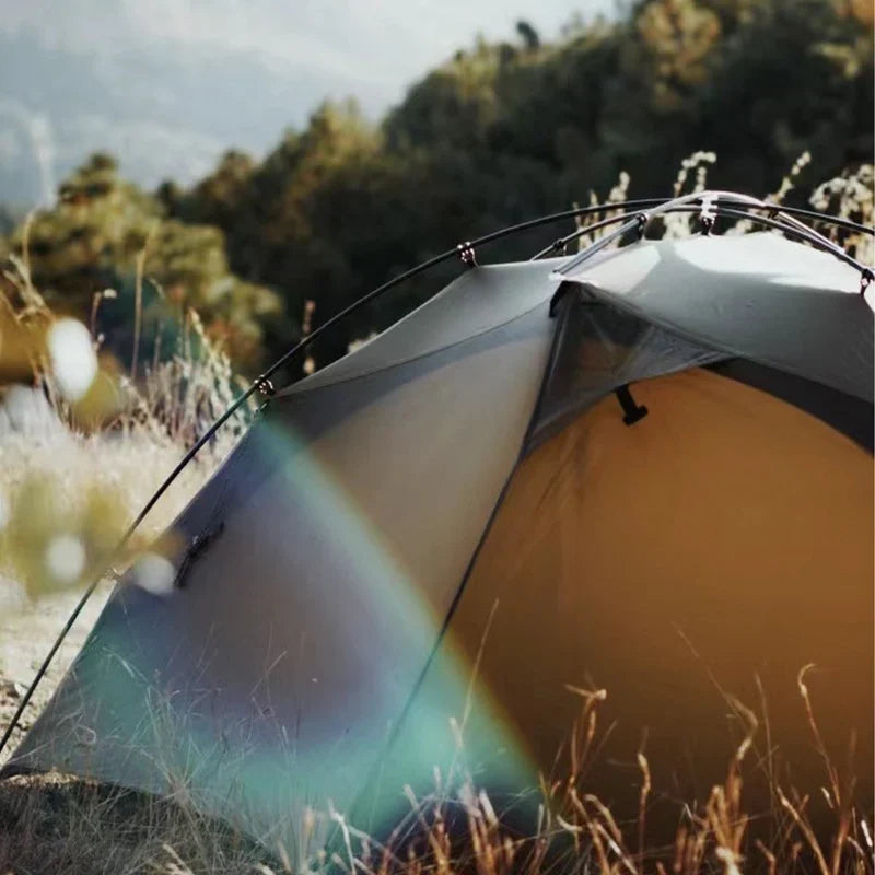 The Free Spirits Goromity Tent in Coyote Tan pitched by a forest with lens flare, close side view.