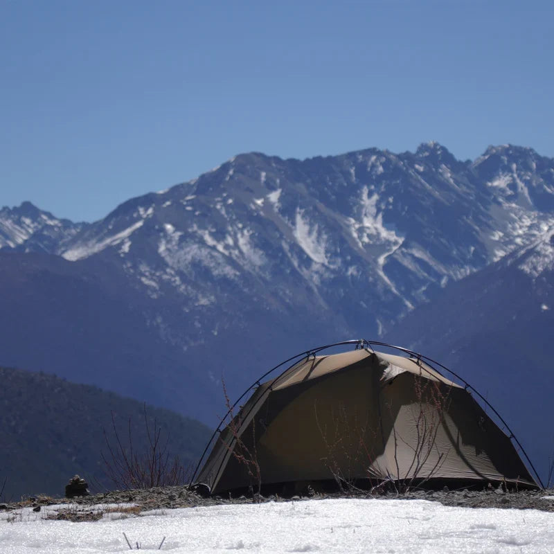 The Free Spirits Goromity Tent in Coyote Tan pitched on snow with magnificent snowy mountains in the background.