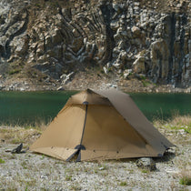 The Free Spirits Vista Tent in Coyote Brown pitched beside a lake and rocky cliffs, side view.