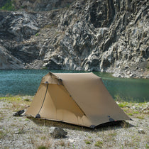 The Free Spirits Vista Tent in Coyote Brown pitched by a lake against rocky cliffs, front view.