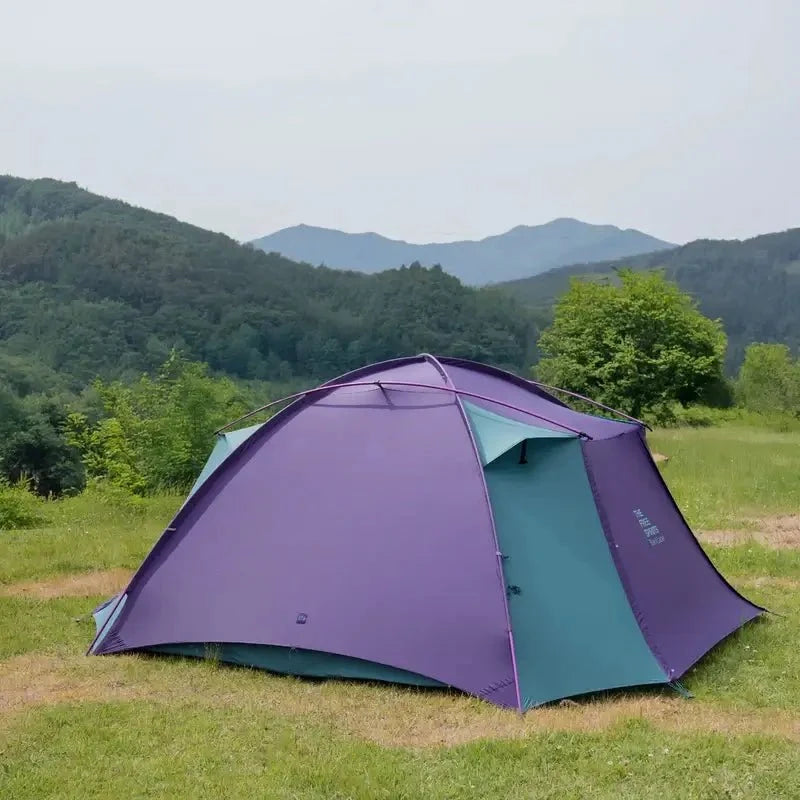 TFS Stars 4 tent in Royal Purple pitched on a green meadow with forested mountains in the background.